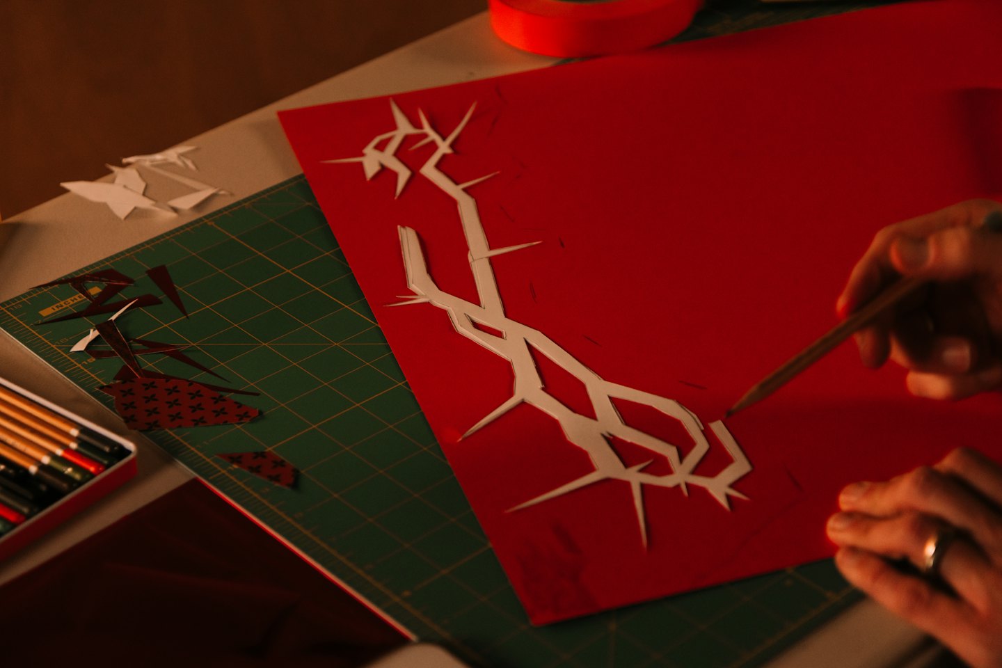 Mani che tagliano con cura un disegno di carta su un tappetino verde.