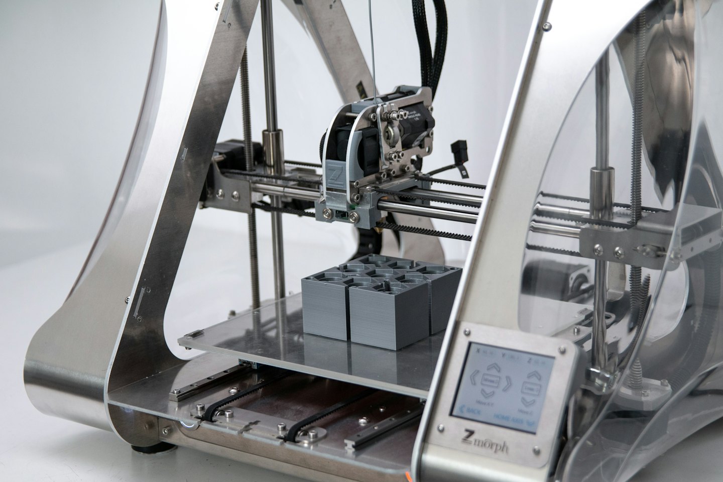 Una stampante 3D crea oggetti grigi sulla sua piattaforma.