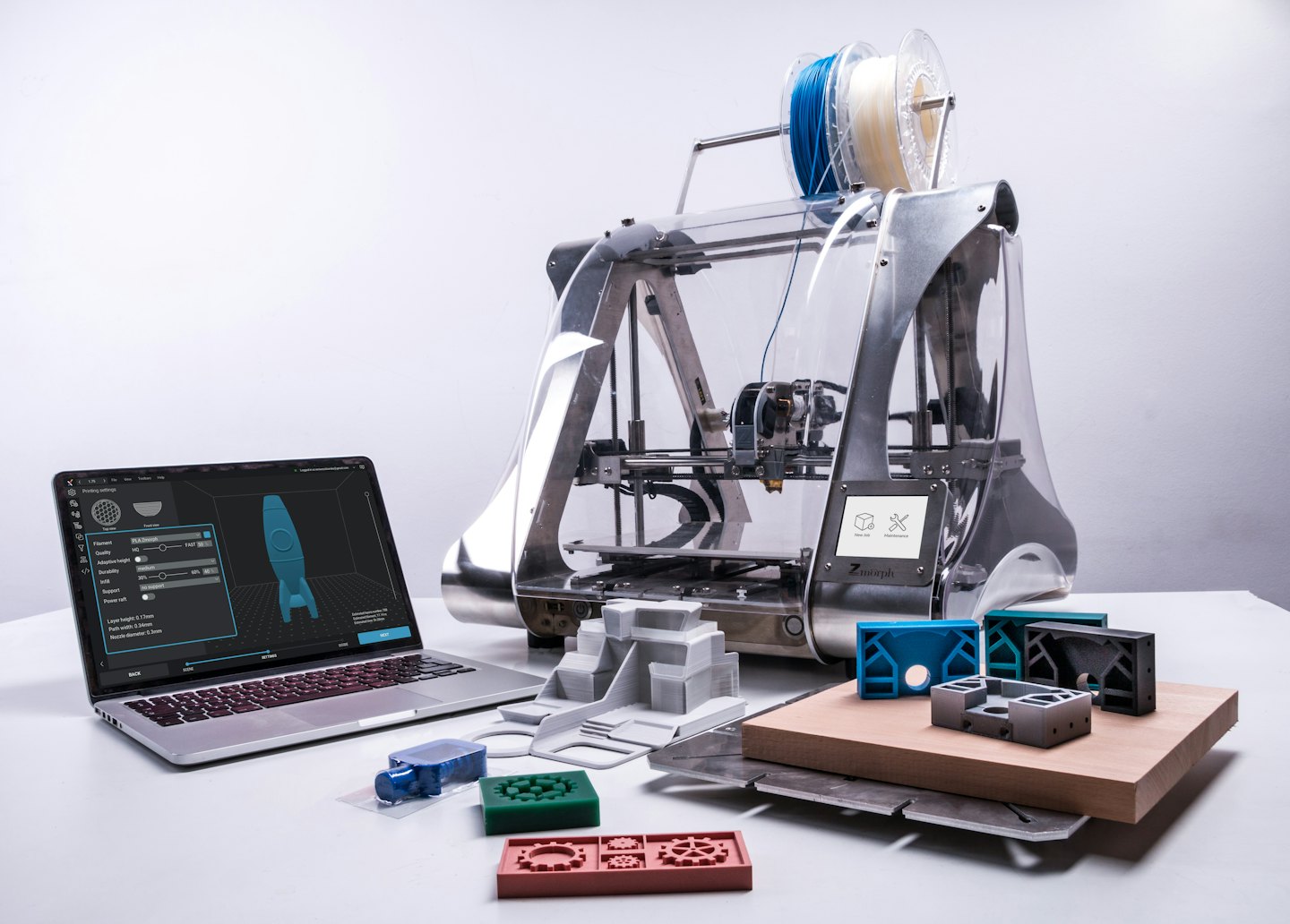 Stampante 3D che crea un modello di razzo accanto a oggetti stampati.