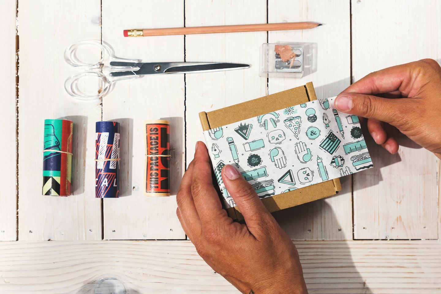 Mani che incartano con cura una piccola scatola con carta velina fantasia.